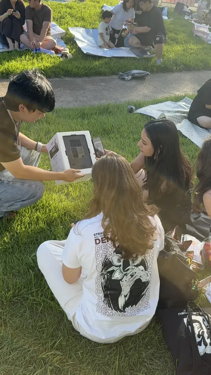 People on picnic blankets at Yeouido Hangang Park taking a photo with a my4cut tablet