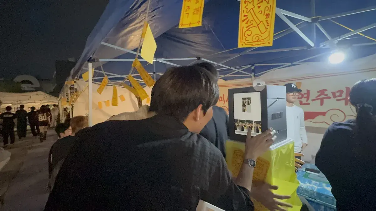 Students shooting with a my4cut mini photo booth on a table under a campus festival tent at night
