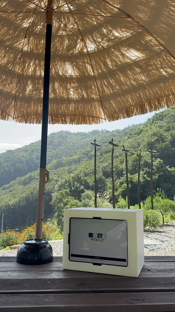 A white my4cut mini photo booth on an outdoor table with mountains behind